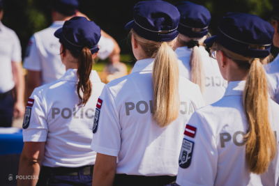 No mugurpuses redzamas vairākas Valsts policijas koledžas kadetes formastērpos ar uzrakstu 'POLICIJA' uz muguras. Viņas stāv rindā, valkājot baltus krekliņus ar Latvijas karodziņu un koledžas emblēmu uz piedurknes, kā arī tumši zilas cepures.